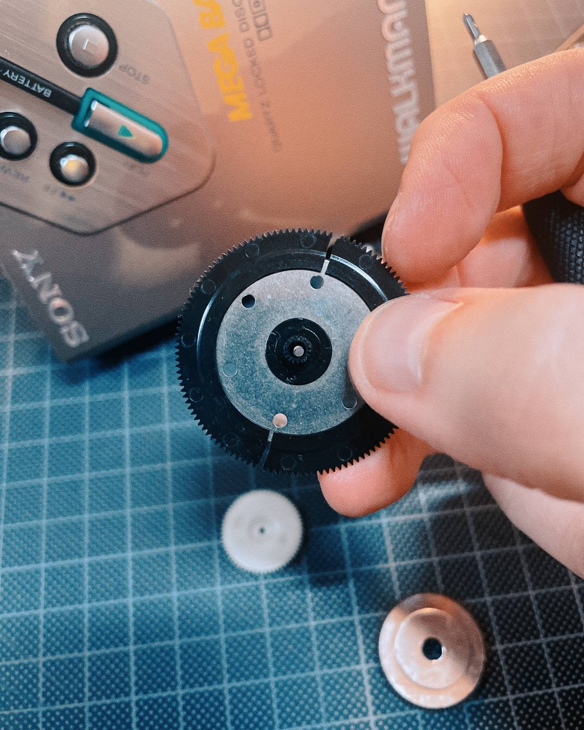 A hand holding a gear while epairing an old Sony walkman